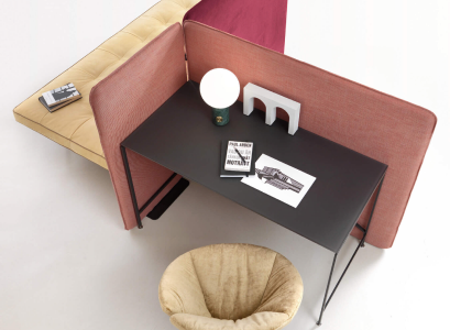 Dark desk with a lamp and books beside a red upholstered partition and pale stool
