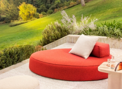 Curved red outdoor sofa with pale cushions beside a green garden