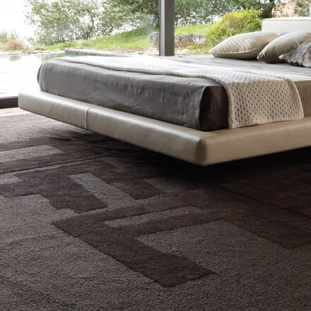 Textured dark rug beneath a low bed beside garden windows