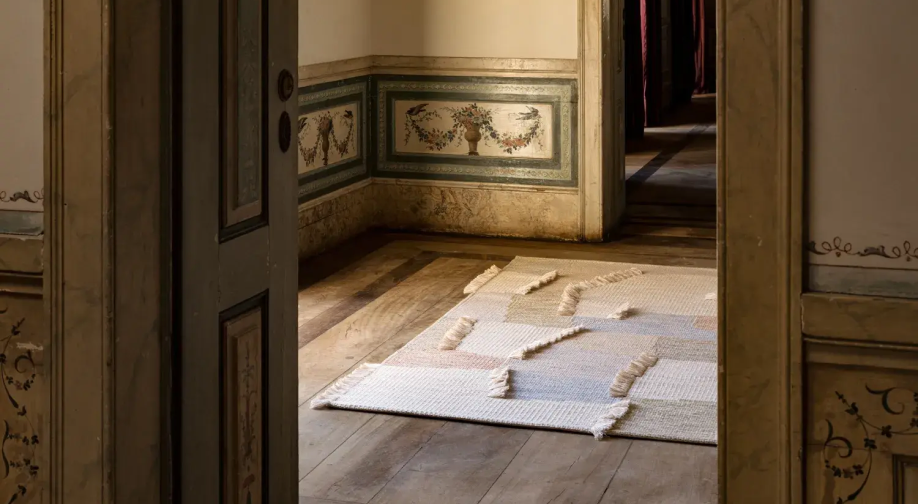 Cream geometric rug with raised woven textures on a wooden floor, viewed through an ornate doorway.